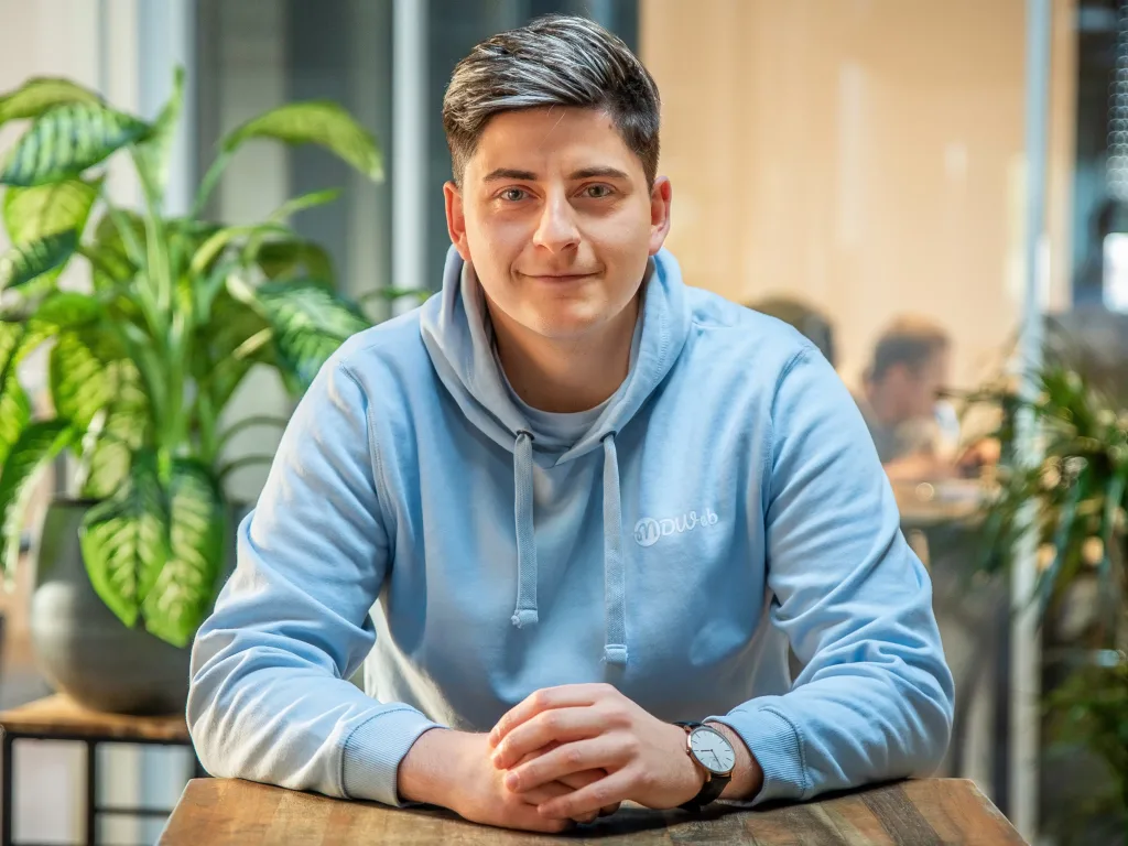 Jeune homme souriant en sweat bleu dans un espace de coworking