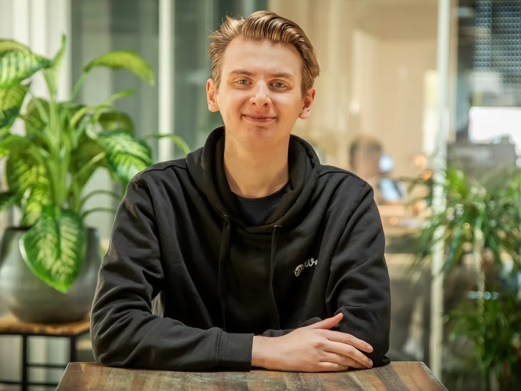 Jeune homme souriant en sweat noir dans un espace de coworking