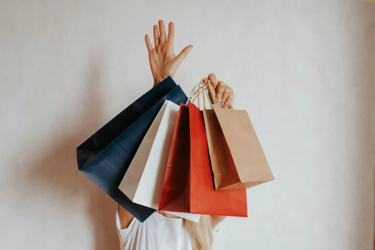 Une personne levant les bras, cachée derrière plusieurs sacs de shopping, illustrant la réussite d'un achat en ligne après avoir su optimiser le tunnel d'achat.